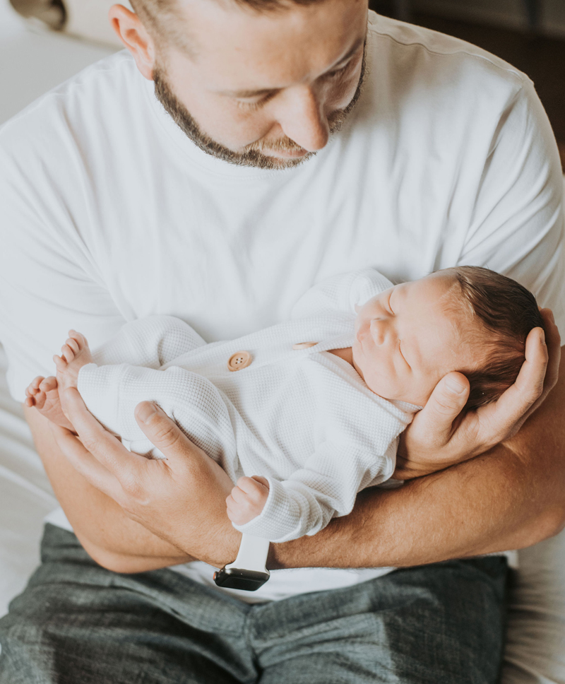 Newborn Photographer, a father holds his baby son in his arms, admiring him