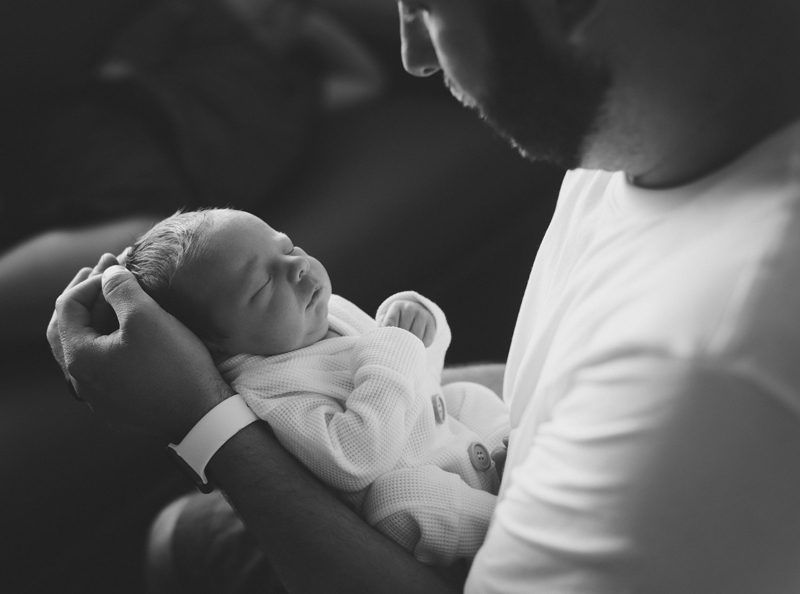 Newborn Photographer, a father holds baby securely in his arms as baby sleeps cozily