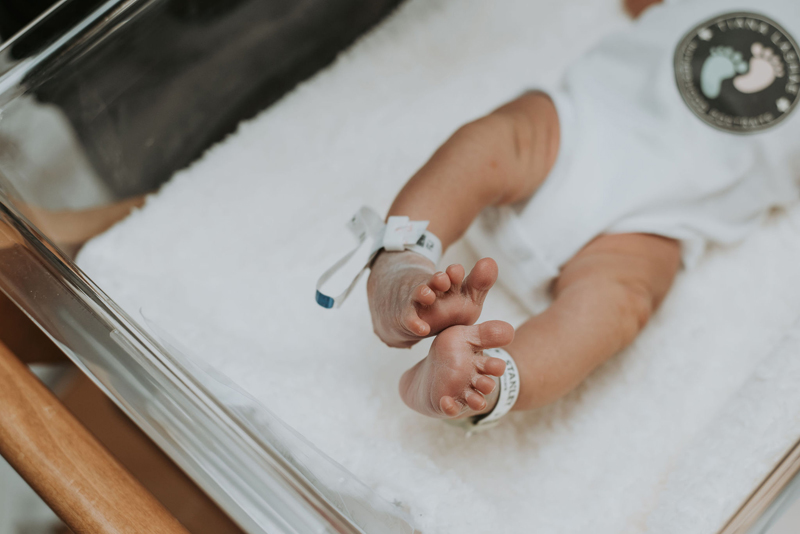 Newborn Photographer, a baby lays in a hospital cradle, little toes curl and hospital anklets on his ankles