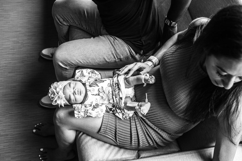 Newborn Photographer, a mother sits on couch with her partner, she holds baby in her lap