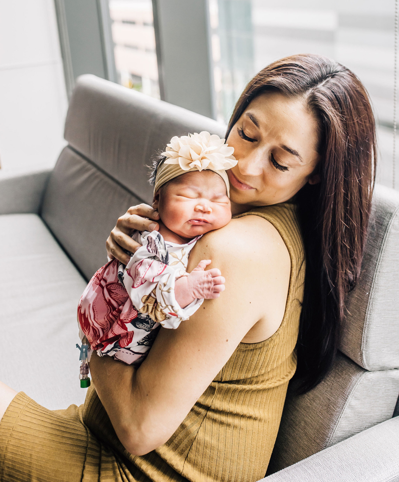 Newborn Photographer, a mother holds her baby girl to her shoulder as she admires her