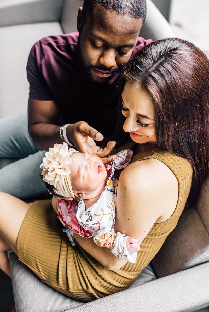 Newborn Photographer, mom holds her newborn baby girl, and dad reaches in to dote on her too, they sit on a hospital couch