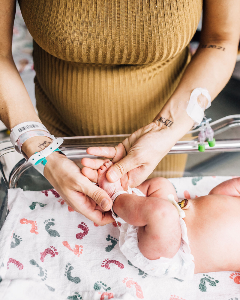 Newborn Photographer,  a mother holds her babies little feet in the hospital cradle