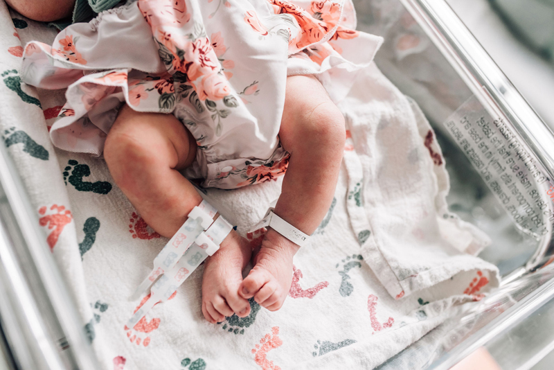 Newborn Photographer, a little baby girl's feet and toes poke out of her floral outfit as she lays on hospital cradle